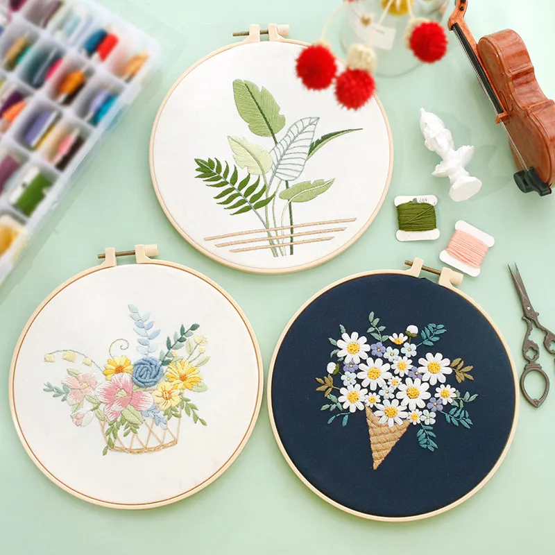 Three floral embroidery hoops with threads and tools on green