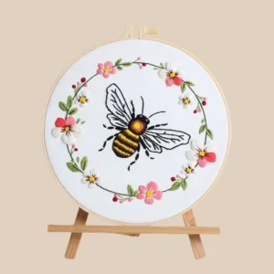 Bee embroidery kit featuring a hand-stitched bee surrounded by a colorful floral wreath, displayed in a wooden hoop with a nature-inspired design.